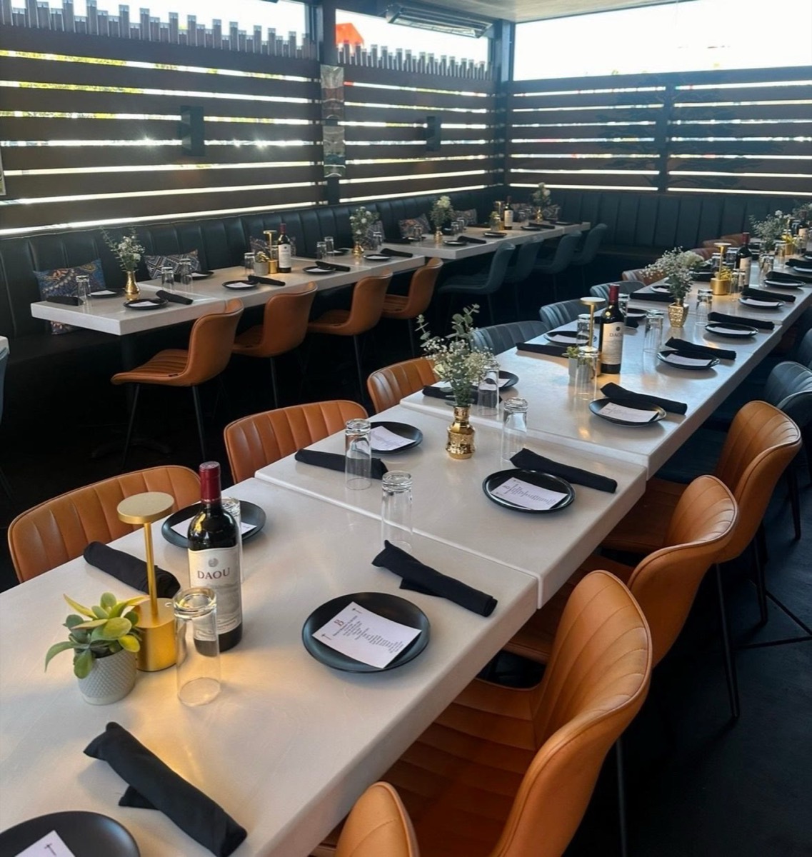 A long table set for a private dinner at Bei with wine, gold lamps and leather chairs